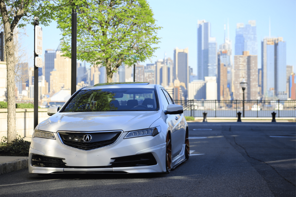 5 Key factors to consider when looking for an Acura auto repair shop in Seekonk, MA with Trustworthy Auto. Image of white acura car parked on side of road with city skyscrapers in the background.