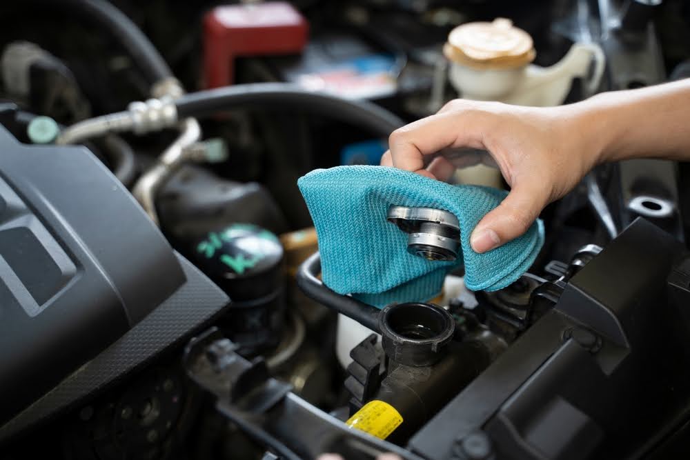 BMW maintenance by Trustworthy Auto in Seekonk, MA: A mechanic's hand using a cloth to check and clean the engine components, emphasizing the importance of regular summer maintenance to prevent overheating.