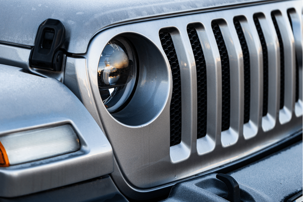 jeep oil cooler leak, auto repair in Seekonk, MA at Trustworthy Auto. Close-up of a silver Jeep’s signature seven-slot grille and round headlight with clear lens and rugged styling.