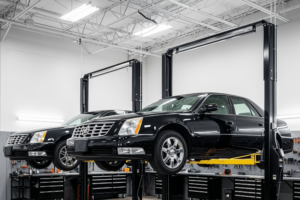 Cadillac Repair & Maintenance, auto repair in Seekonk, MA at Trustworthy Auto. Two black cars lifted on hydraulic car lifts inside a brightly lit auto repair shop, with tool cabinets and equipment visible in the background.