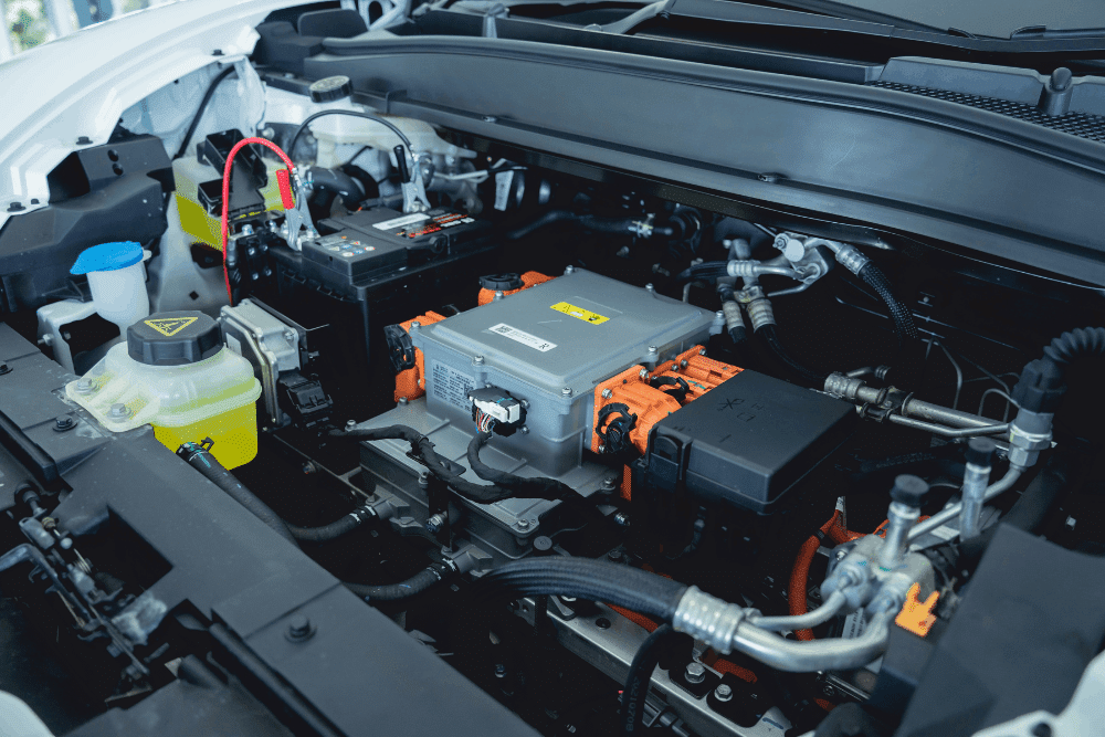 Auxiliary battery, Hybrid & EV repair in Seekonk, MA at Trustworthy Auto. Image of an engine bay with high-voltage orange cables, electrical components, a battery, and fluid reservoirs for inspection and maintenance.